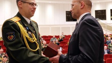 Военнослужащий в парадной форме вручает награду мужчине в костюме в зале