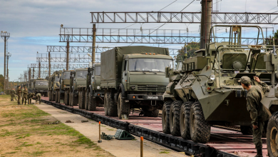 Военные грузовики и бронетранспортёр на платформах, военнослужащие у состава
