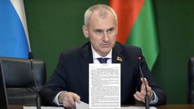 Мужчина в костюме показывает документ на фоне флагов России и Беларуси
